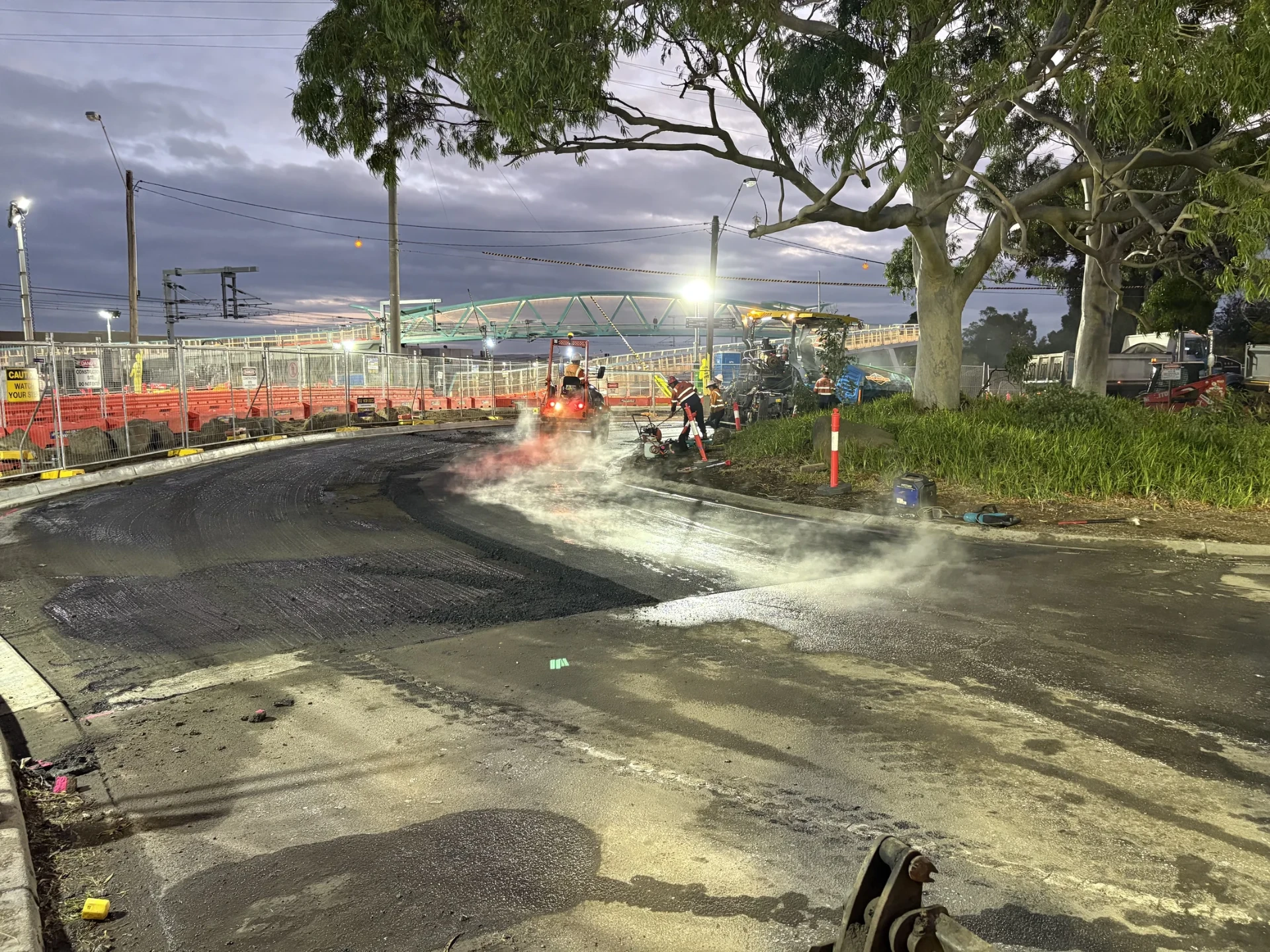 Asphalt paving crew and plant completing a surfacing shift under lights at night.